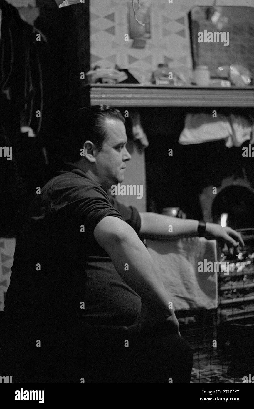 Man sat having a cigarette in front of a cast iron cooking range, during the slum clearance and demolition of St Ann's, Nottingham. 1969-1972. Stock Photo