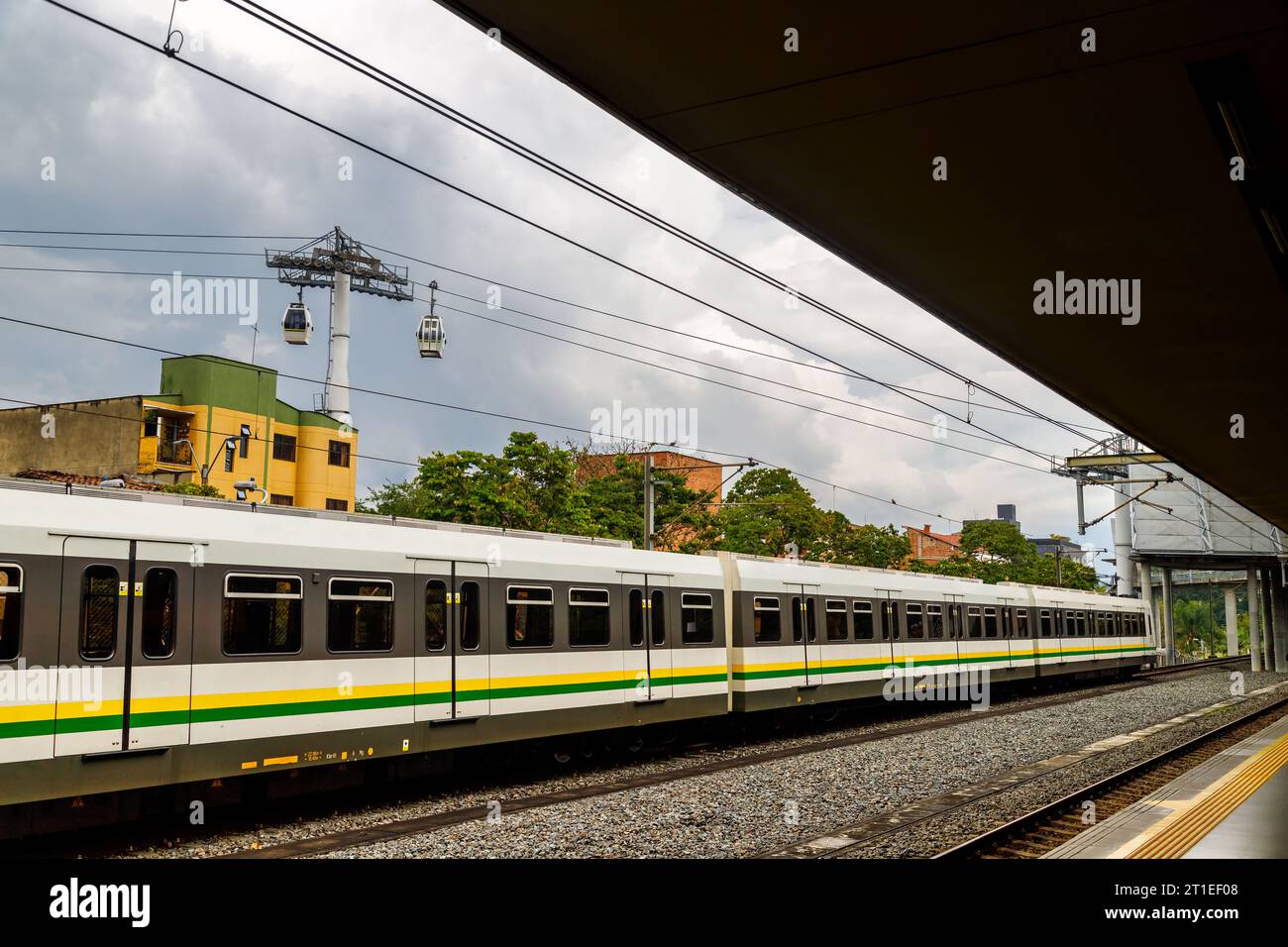 Medellin metro leaving a station with metrocables in the background Stock Photo