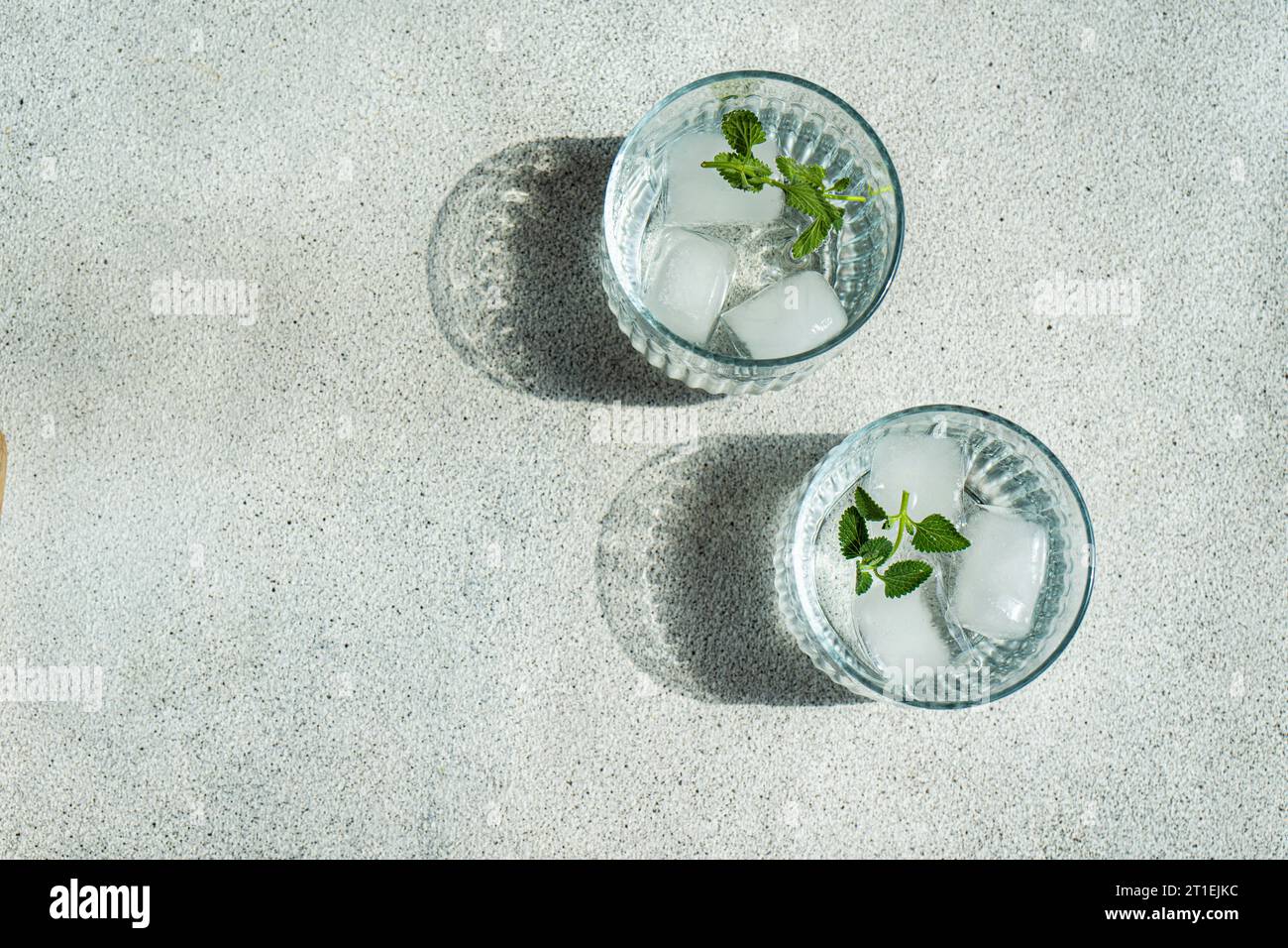 Drinking water with mint leaves and ice cubes on concrete table Stock Photo