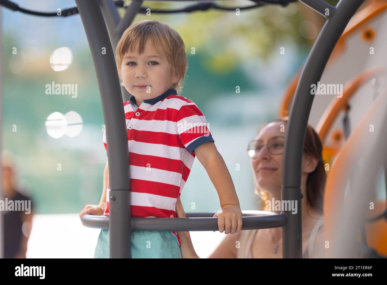 Cute blond boy climbing ladder on playground with support of his ...