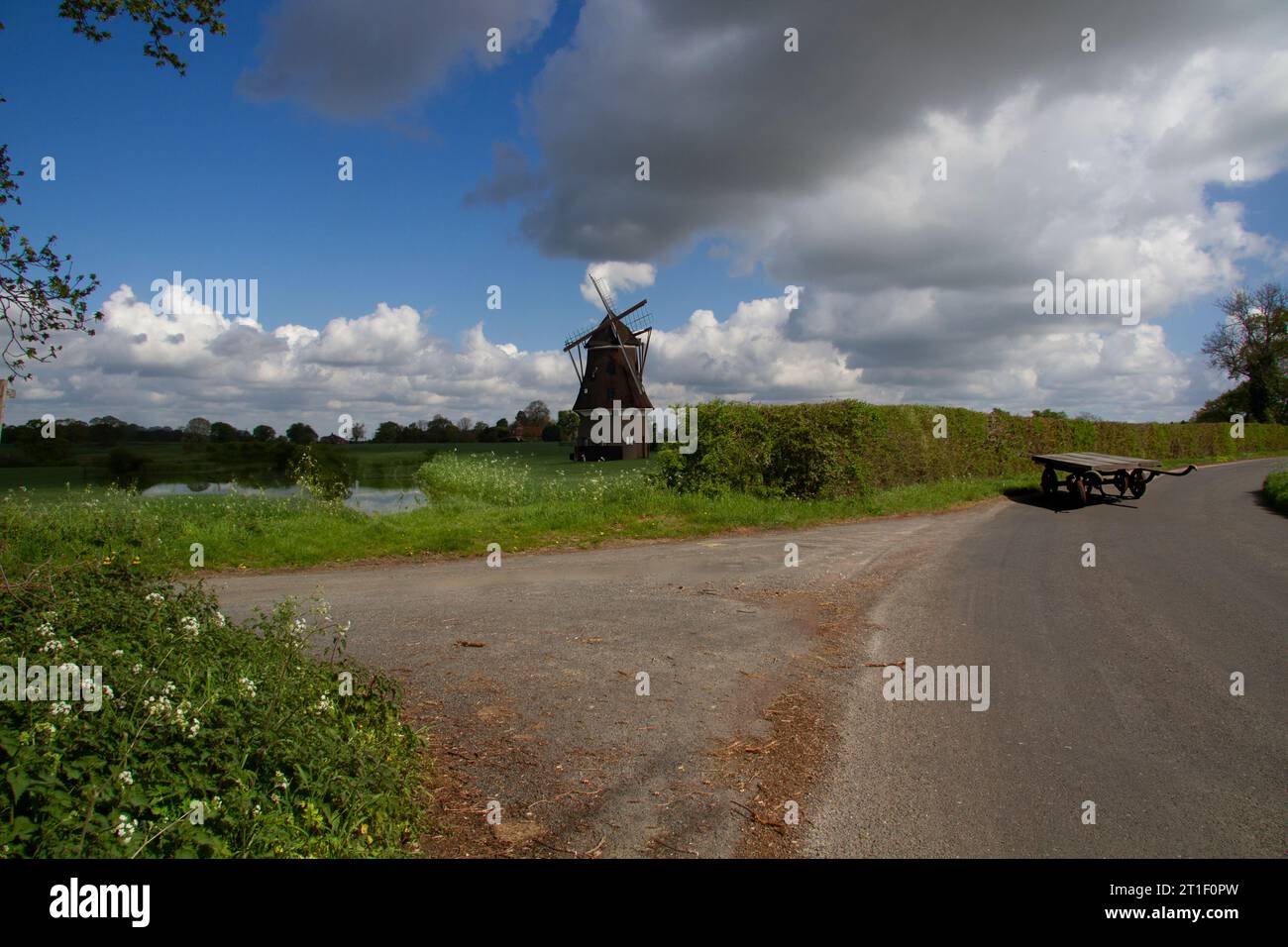A rural landscape setting in Essex with a windmill near a pond, by a lane with an old wooden cart Stock Photo