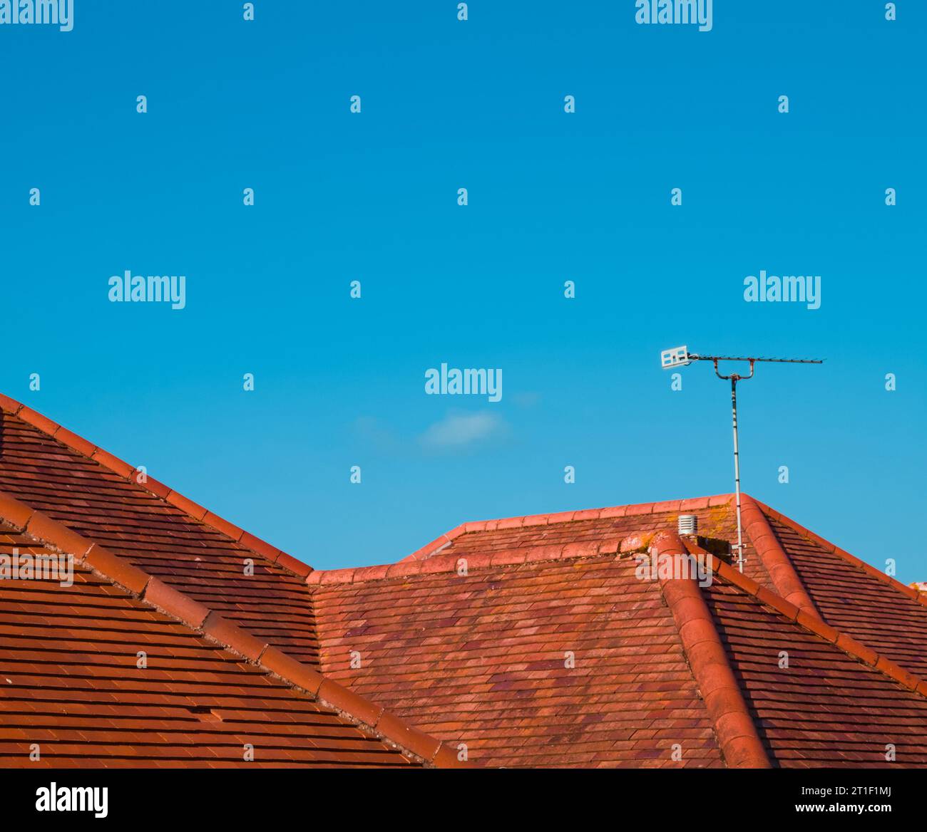 Terracota Tiled Roofs With A Television Antenna Set Against A Blue Sky Imitating Mountains In A Landscape, UK Stock Photo