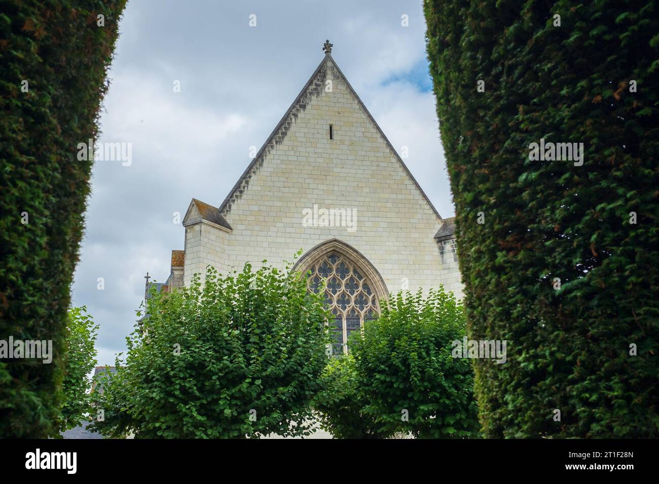 Angers, France, 2023. In the formal garden, the 15th century chapel and its stained glass window can be seen through the arch of a yew topiary Stock Photo