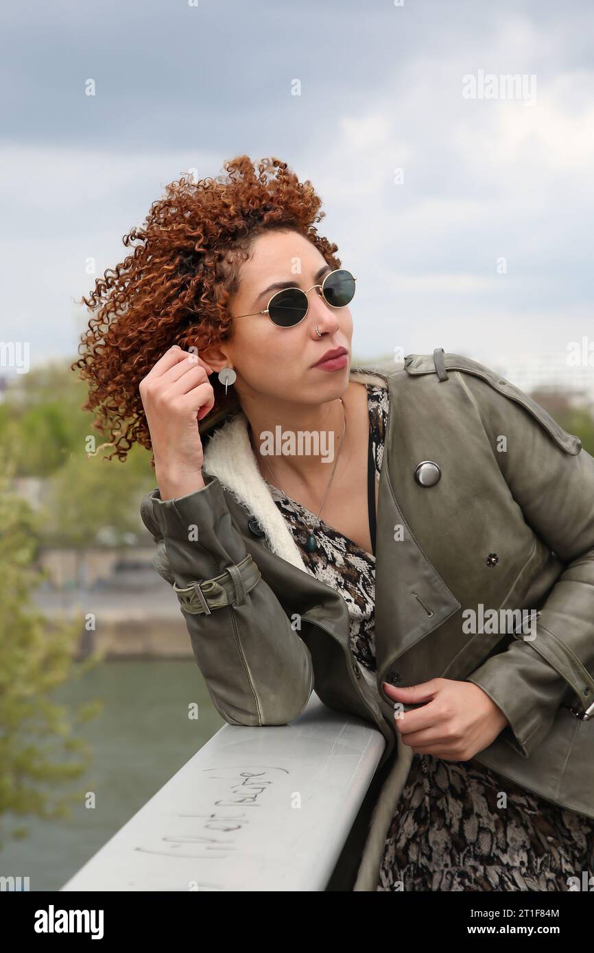 Curly hair woman with green trench coat and black sunglasses looking on the side Stock Photo