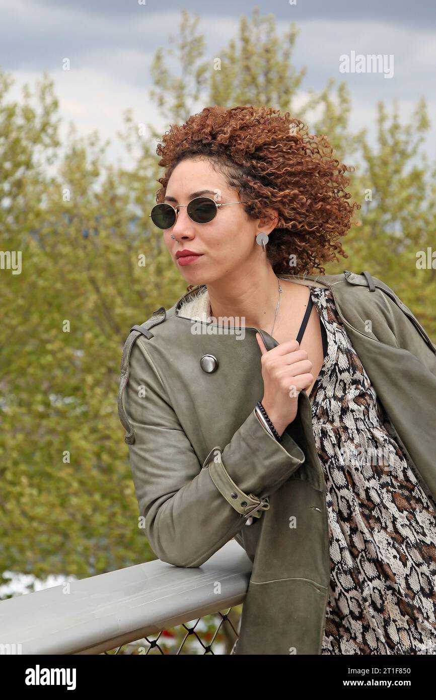 Curly hair woman with green trench coat and black sunglasses looking on the side Stock Photo
