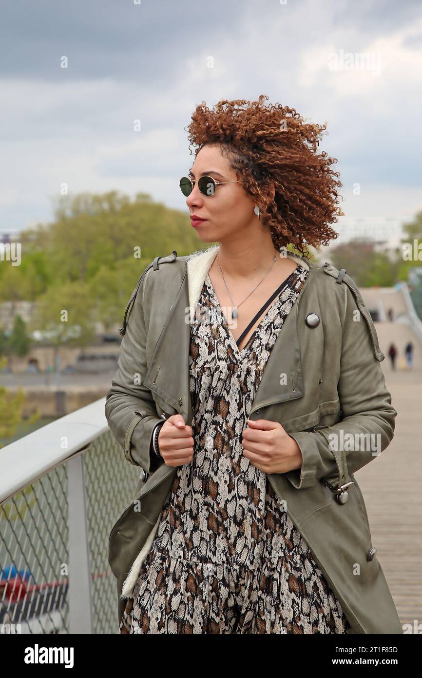 Curly hair woman with green trench coat and black sunglasses looking on the side Stock Photo