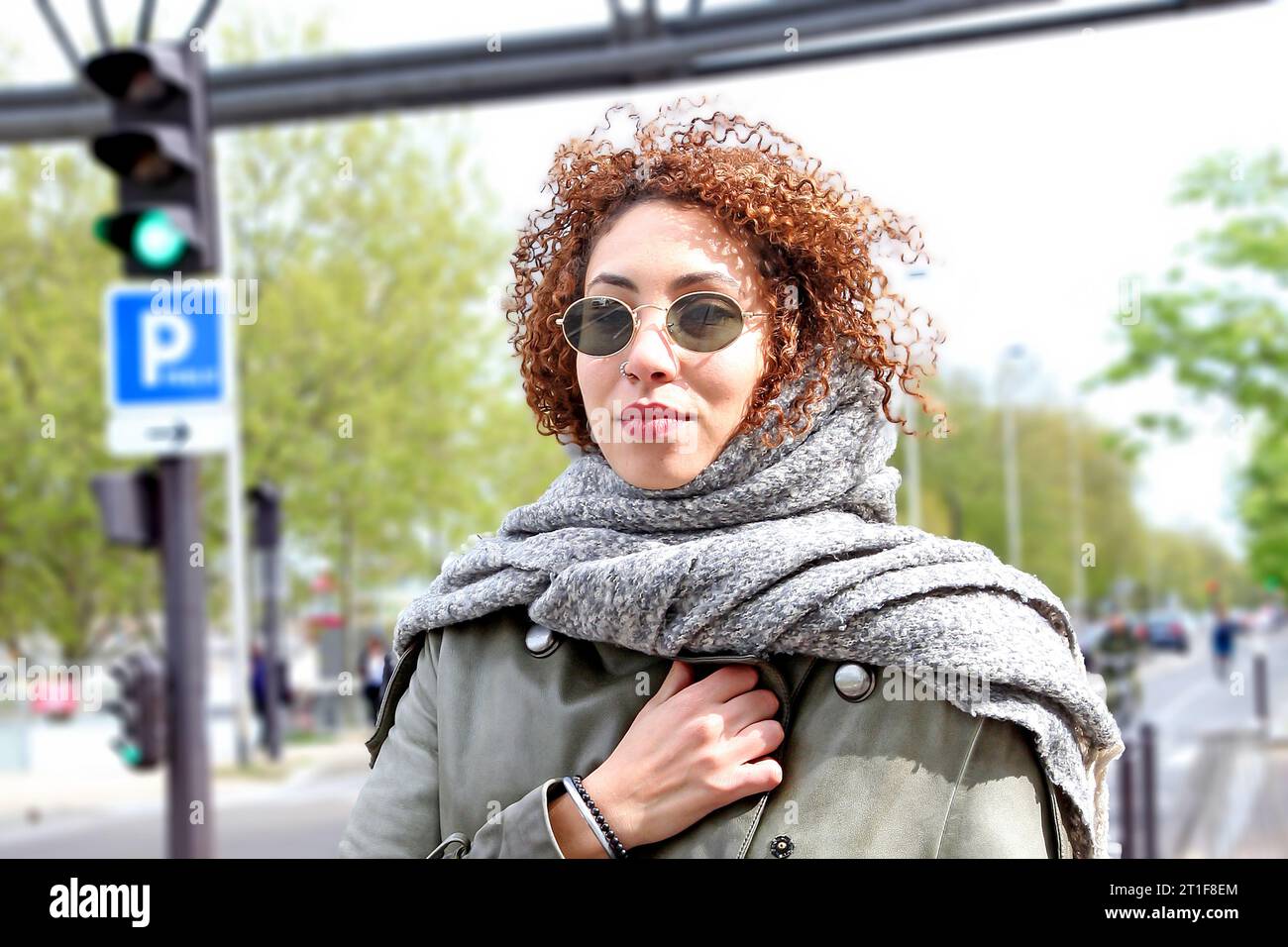 Curly hair woman with green trench coat scarf and dark sunglasses posing in streets of paris near green light Stock Photo