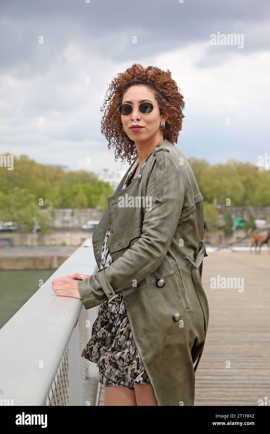 Curly hair woman wearing  a green trench coat and sunglasses looking at the camera Stock Photo