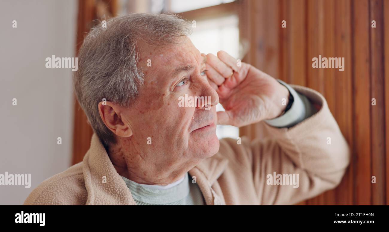 Depression, sad or nostalgia with a senior man looking through a window in his home during retirement. Thinking, memory or the past with an elderly Stock Photo