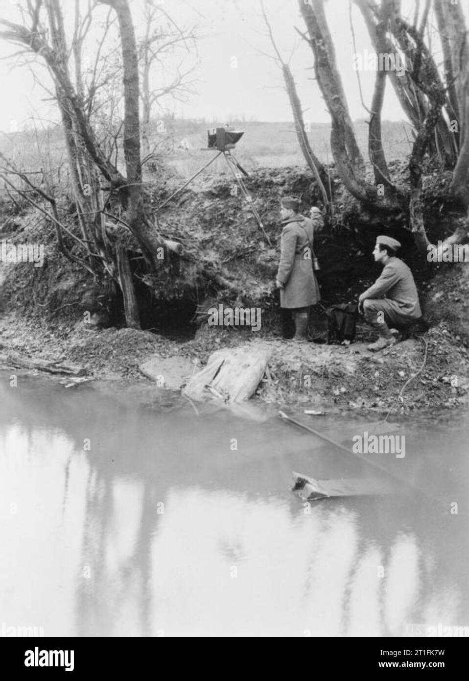 First World War Photographers An American official photographer of the US Signal Corps and his assistant carry out reconnaissance photography under cover of a deep river bank by the River Aire on the Western Front. They are using a glass plate camera mounted on a tripod to photograph the German lines. Stock Photo