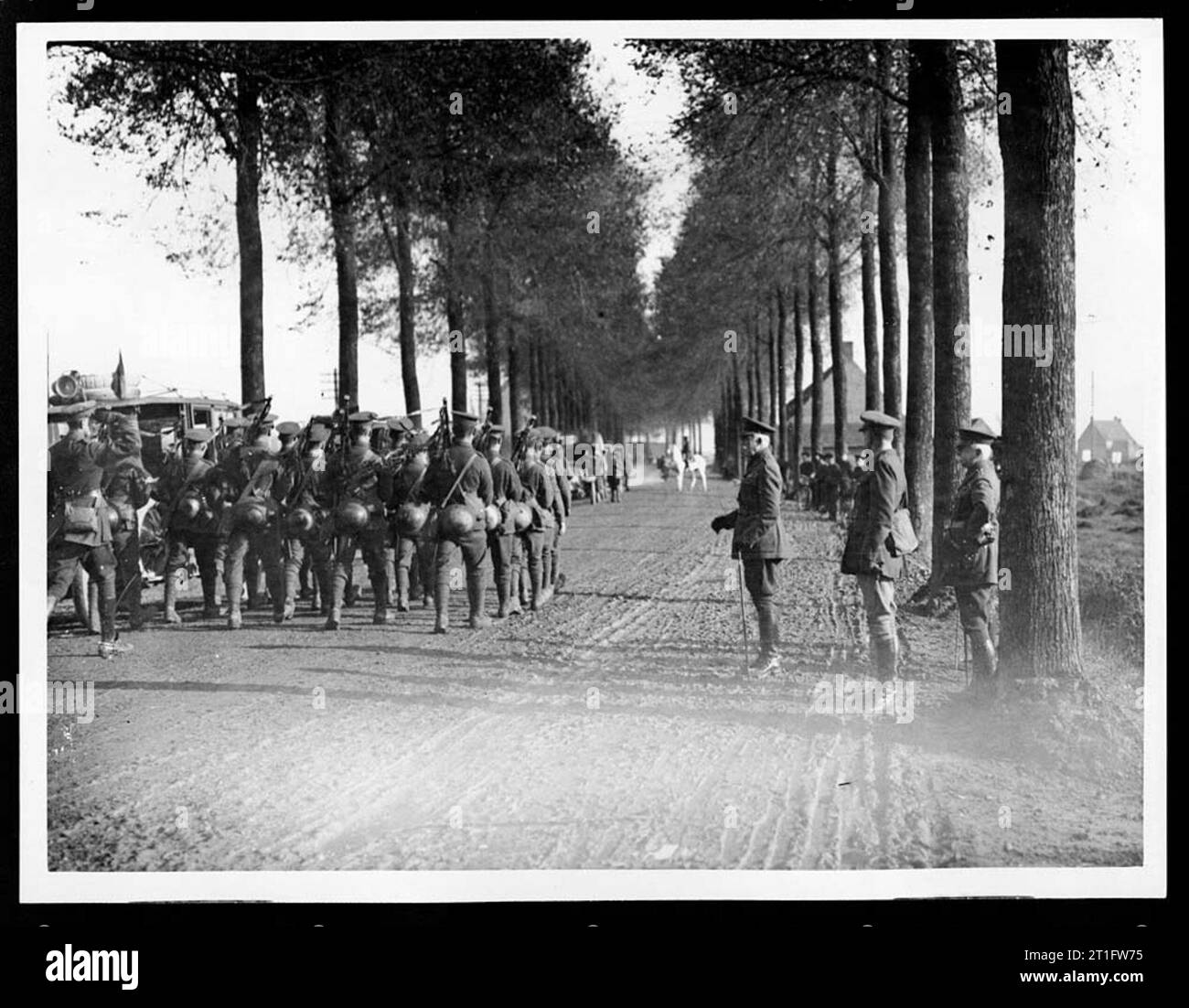 Photographs of royal visits to the Western Front. Royal visits were seen as an important way of boosting morale. Irish troops march along a dusty tree-lined road. Some of the troops are playing the bagpipes. Onlookers watch from the side of the road. In the distance are a number of vehicles and a man on a grey horse. The Duke of Connaught was Queen Victoria's third son. General Plumer was celebrated for leading the successful Battle of Messines Ridge in 1917. [Original reads: 'OFFICIAL PHOTOGRAPH TAKEN ON THE WESTERN FRONT - Irish troops march past the Duke of Connaught and General Sir Herbert Stock Photo