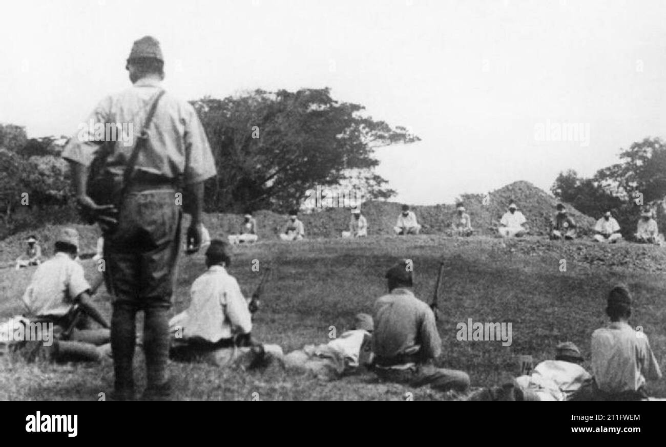 ATROCITIES CARRIED OUT BY JAPANESE FORCES DURING THE SECOND WORLD WAR WAR OFFICE, CENTRAL OFFICE OF INFORMATION AND AMERICAN SECOND WORLD WAR OFFICIAL COLLECTION. This set of four atrocity pictures was found among Japanese records when British troops entered Singapore. Picture shows:- This shows Japanese soldiers loading their rifles and getting ready to shoot their Sikh prisoners, who are seated, blindfolded in a rough semi-circle, 20 yards away. Stock Photo