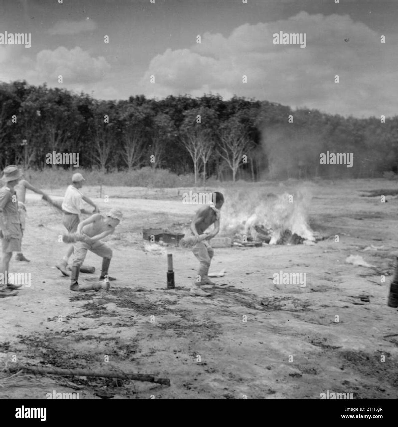 The British Reoccupation of Malaya Japanese prisoners of war throwing incendiary bombs onto a fire that already contains cases of cordite from the former Japanese ammunition store in the limestone caves at Batu, Selangor State, near Kuala Lumpur. Stock Photo