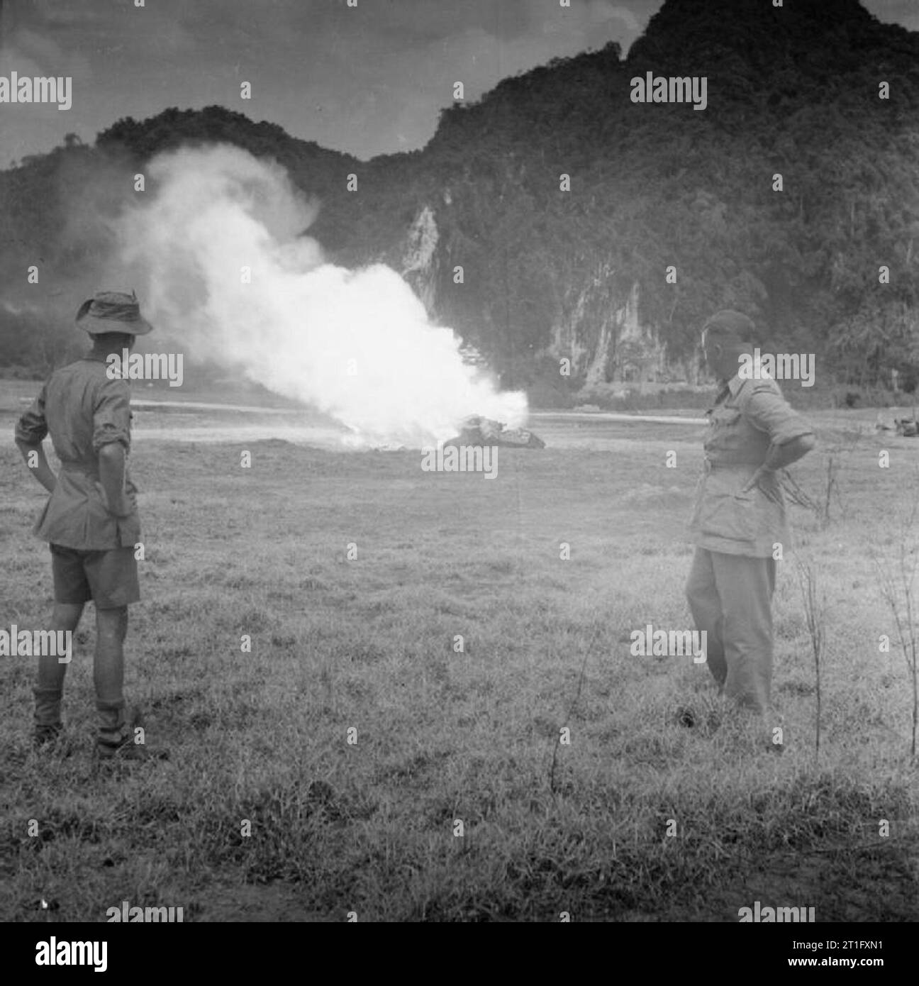 The British Reoccupation of Malaya Two British officers watch as a fierce magnesium flame leaps into the air as an incendiary bomb ignites on a fire formed by burning munitions from the former Japanese ammunition store in the limestone caves at Batu, Selangor State, near Kuala Lumpur. Stock Photo
