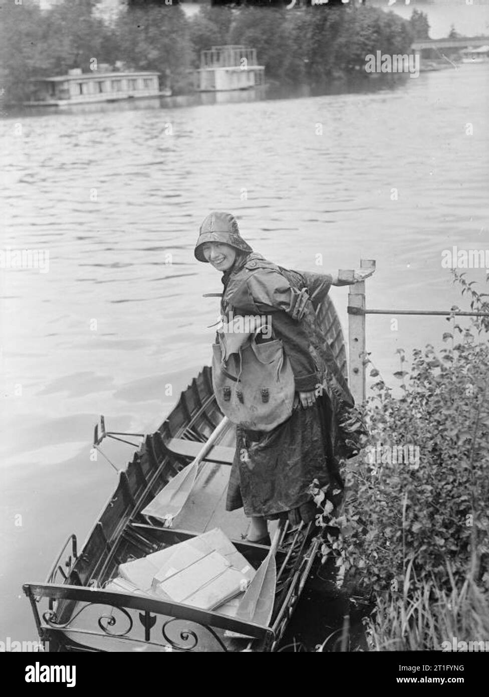 Women at work during the First World War A river postwoman smiles for the camera as she steps into her rowing boat from the bank. She is wearing oilskins and a sou'wester, to protect her from the rain. She is carrying a large sack of mail. Stock Photo