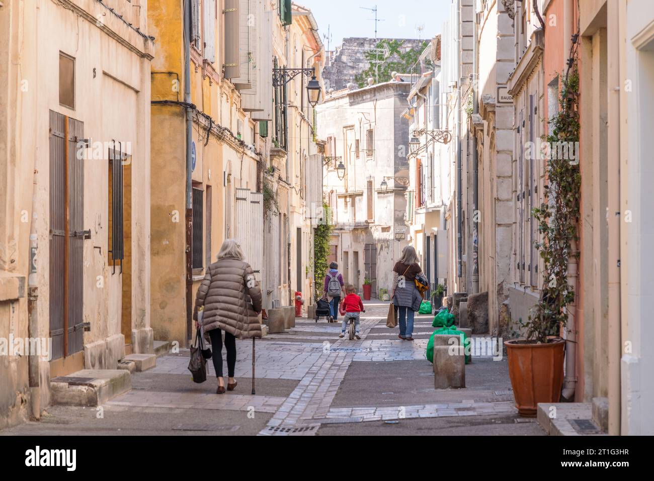 People walk down a narrow pedestrianized street in La Roquette quarter in the old town of Arles in Provence, southern France. No faces are shown. Stock Photo