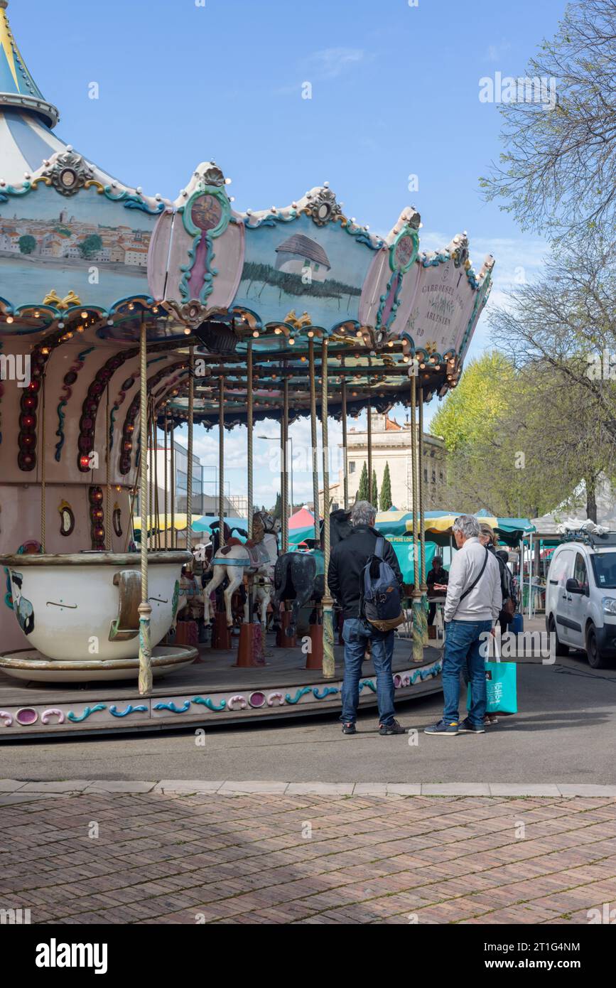 Market goers in conversation next to the children's merrygoround at the Saturday outdoor market in Arles, Provence, southern France. Stock Photo