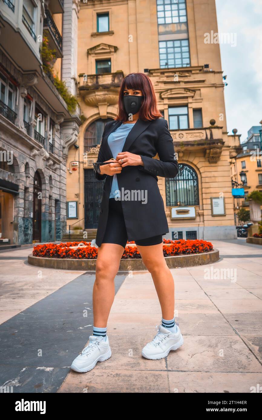 Fashion photo shoot of the new normal, an enterprising young brunette with a face mask leaving work, coronavirus pandemic. Photoshoot in the city Stock Photo