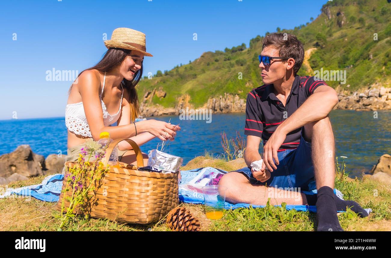 A young couple on a picnic drinking orange juice in the mountains by the sea enjoying the summer Stock Photo