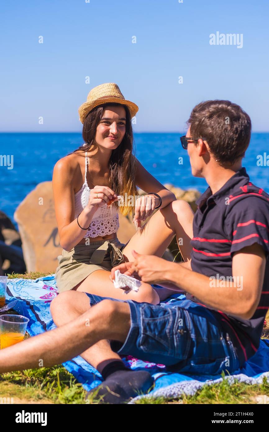 A young Caucasian couple eating some ham at the picnic in the mountains by the sea enjoying the heat, summer lifestyle Stock Photo