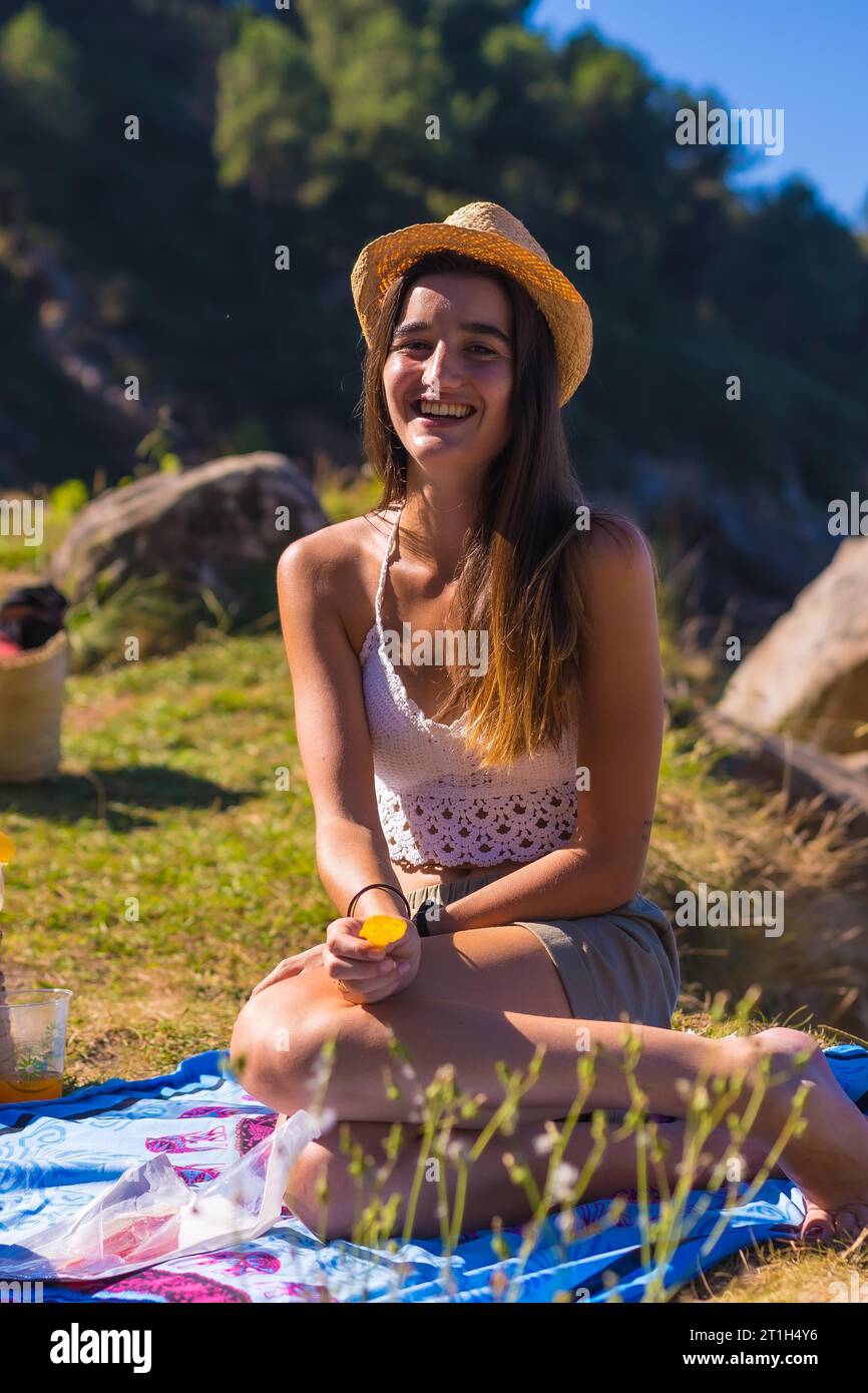 A young Caucasian couple at the picnic eating chips in the mountains by the sea enjoying the heat, summer lifestyle Stock Photo