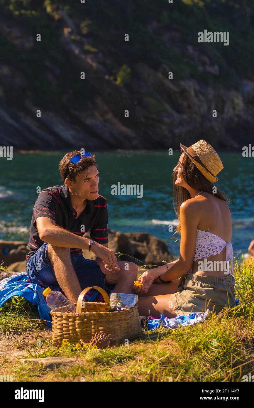 A couple smiling at the picnic in the mountains by the sea enjoying the heat, summer lifestyle Stock Photo