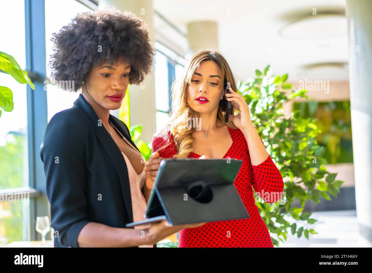 Young enterprising girls, Caucasian blonde and black skinned girl with afro hair making a work video call with a tablet. Lifestyle, working with good Stock Photo