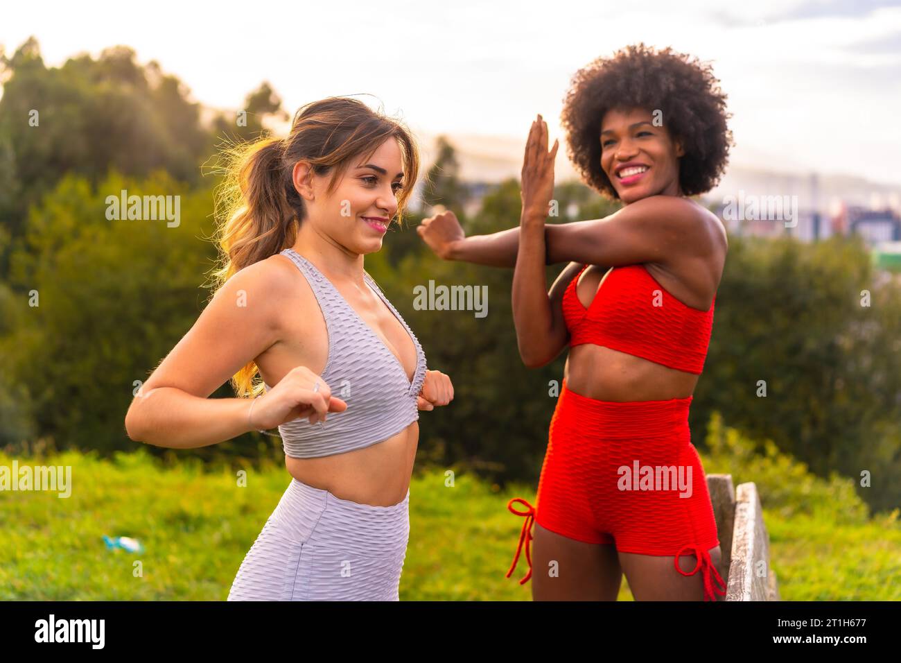 Caucasian blonde girl and dark-skinned girl with afro hair doing stretching before starting sports in the park. Healthy life, fitness, fitness girls Stock Photo