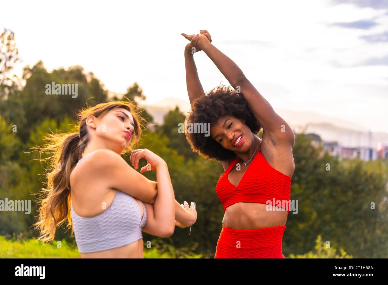 Caucasian blonde girl and dark-skinned girl with afro hair doing stretching before starting sports in the park. Healthy life, fitness, fitness girls Stock Photo