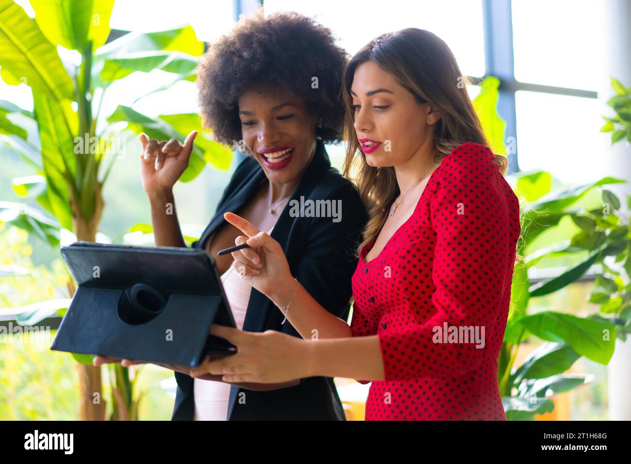 Young enterprising girls, Caucasian blonde and black skinned girl with afro hair making a work video call with a tablet. Lifestyle, working with good Stock Photo