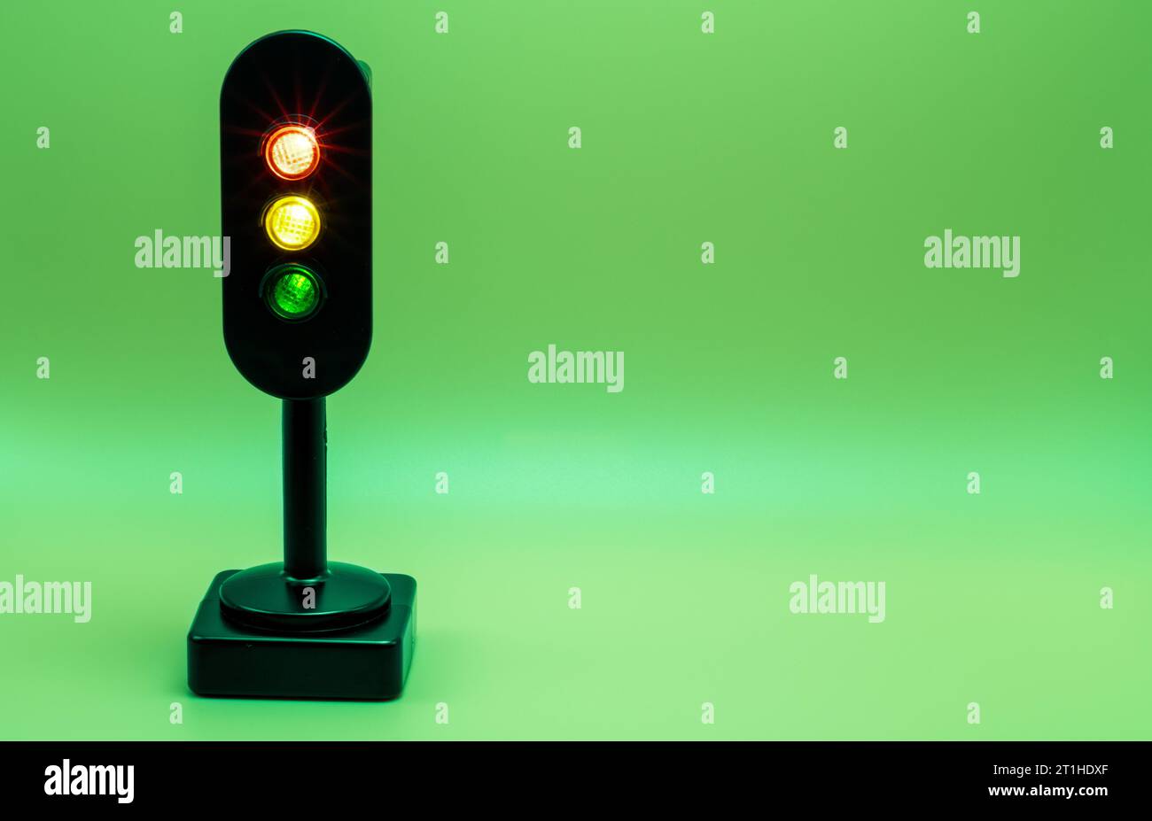 Miniature traffic light with red, orange and green light on. Studio shot. Green empty background. Stock Photo