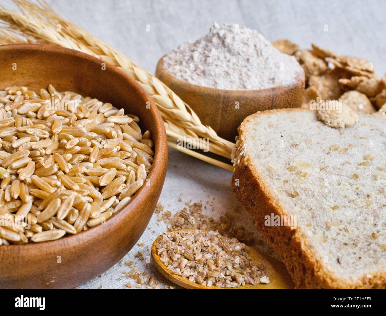 Still life of wheat, whole grain wheat, bulgur wheat, whole wheat flour, and whole wheat bread, with wheat ear on linen table cloth. Stock Photo