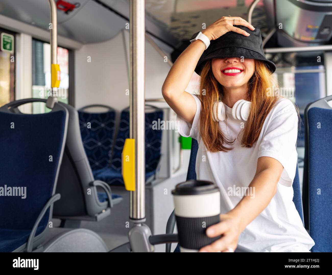 Teen girl covering eyes with her headdress and smiling. Youth culture. Woman inside the bus. Passenger city life and public transportation. Stock Photo