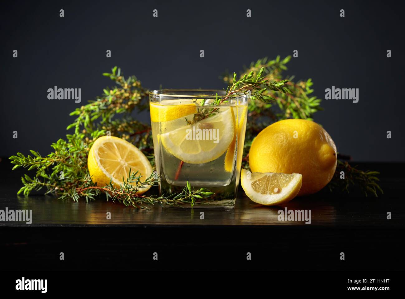 Cocktail Gin-tonic with ice, lemon, and juniper branches on a black wooden table. Stock Photo