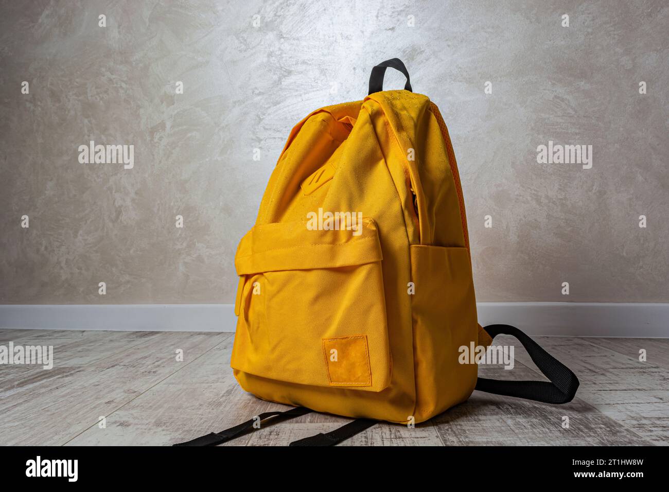 yellow backpack with raindrops on a white wall background close-up Stock Photo