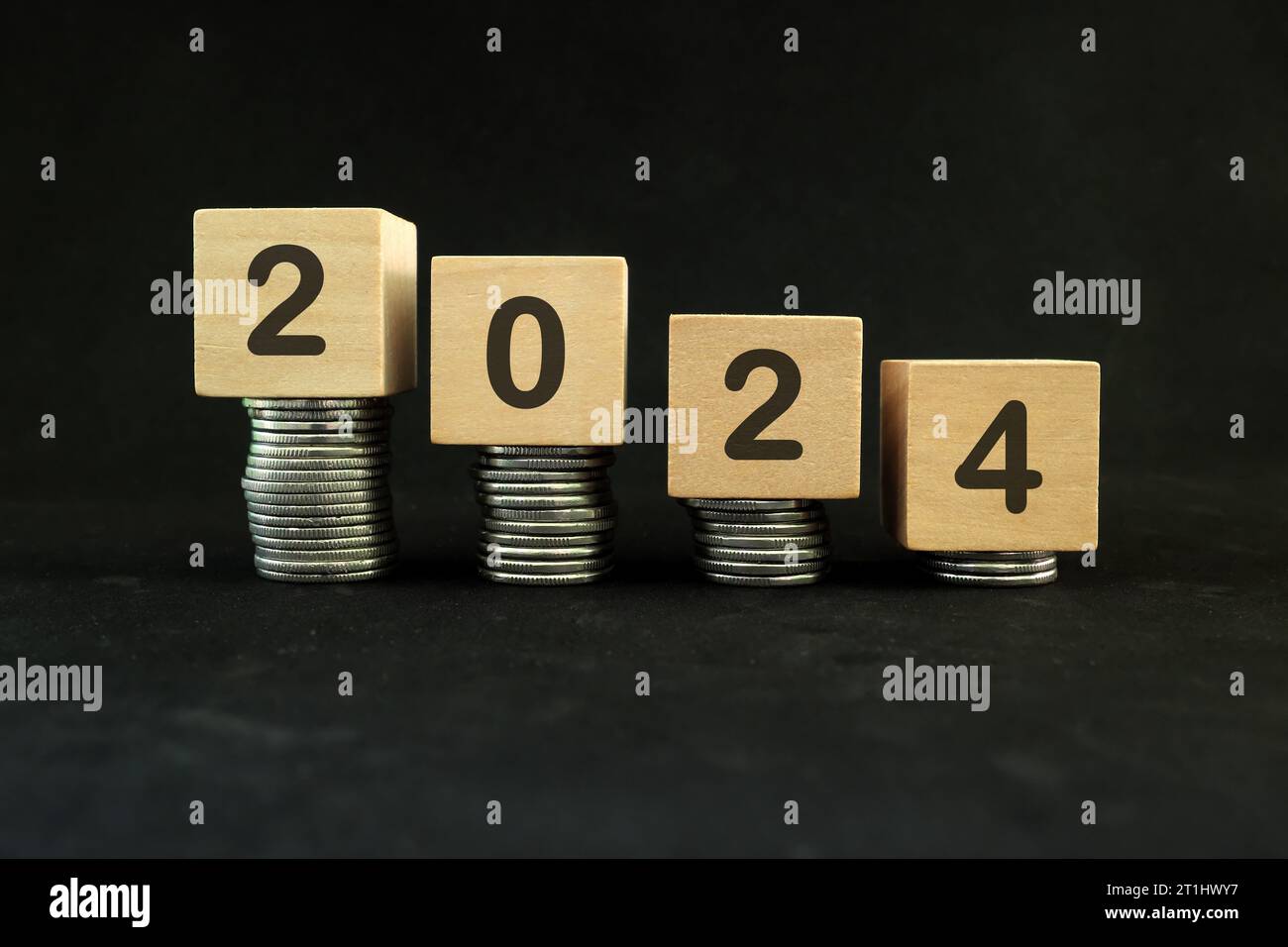 Year 2024 economic recession and crisis concept. Decreasing stack of coins in dark black background. Stock Photo