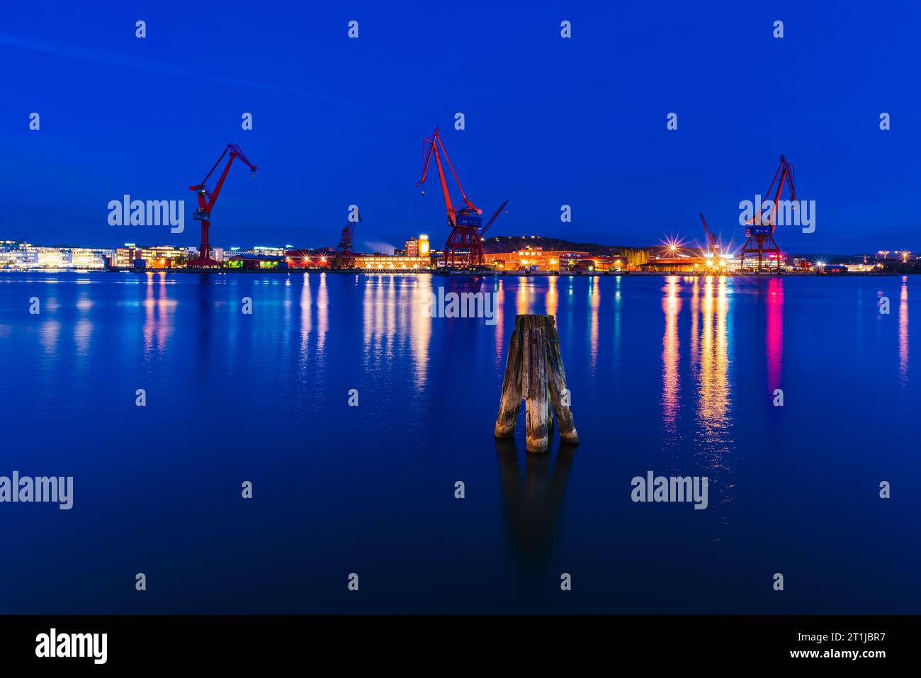 Blue evening sky over illuminated Gothenburg harbor with cranes and machinery. Stock Photo