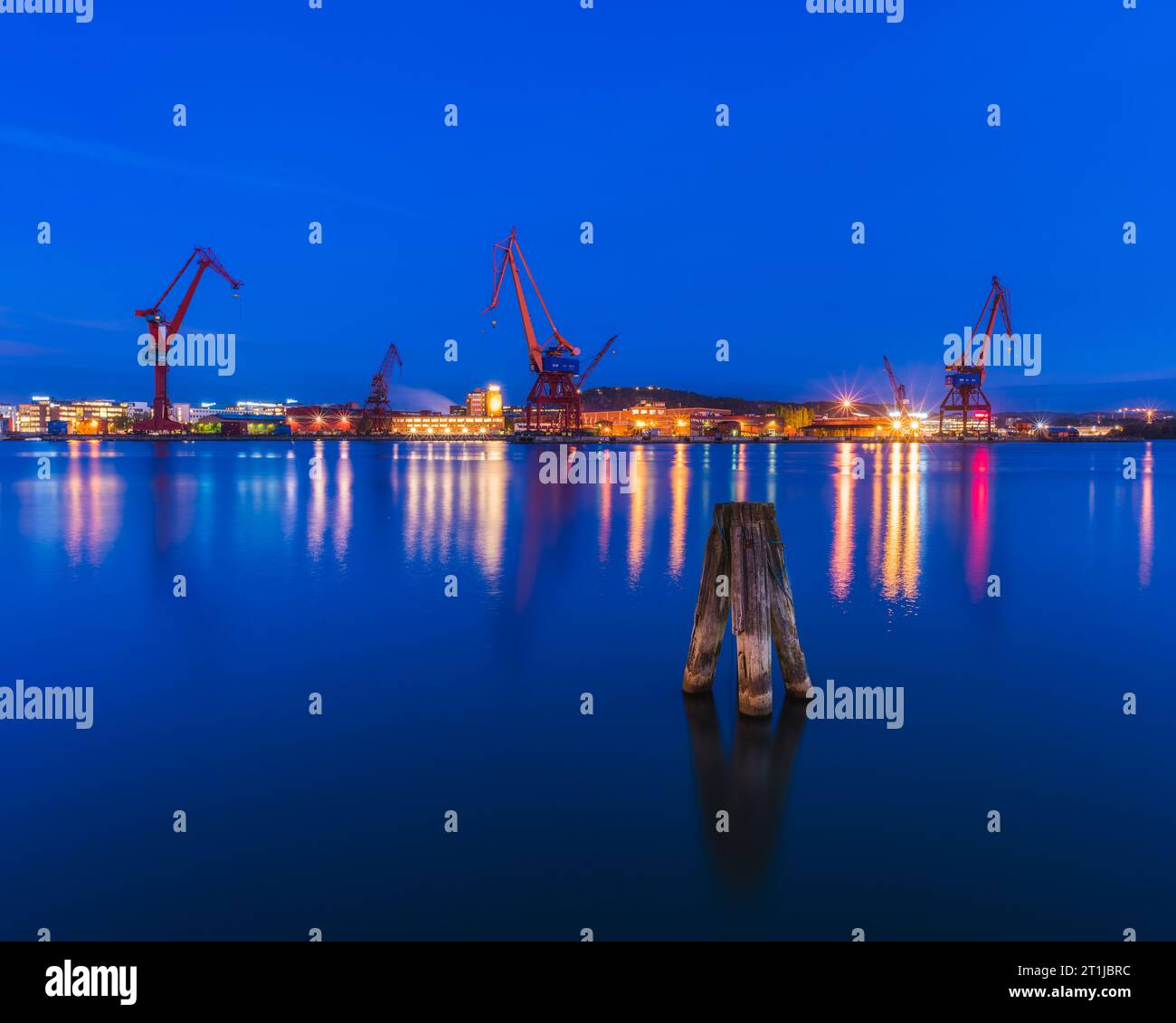 Blue evening sky over illuminated Gothenburg harbor with cranes and machinery. Stock Photo