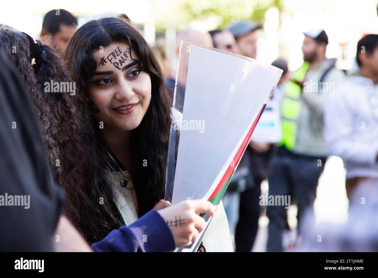 Free Palestine protest Exeter city centre - young Palestinian looking lady with hash tag '#FREEPALESTINE' black writing on forehead of face Stock Photo