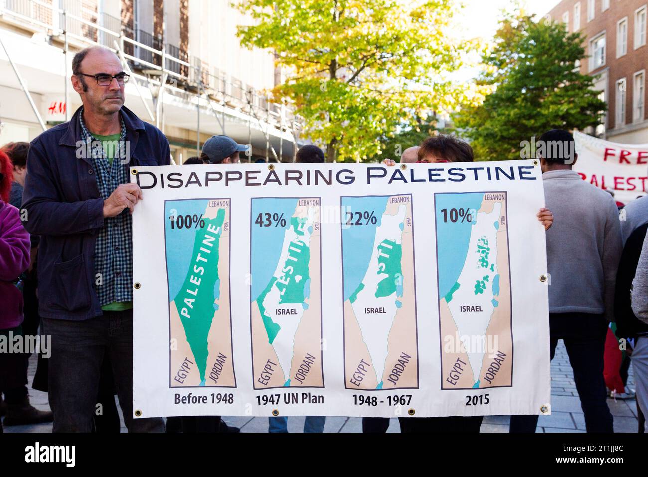 Free Palestine protest Exeter city centre - gentleman and hidden lady holding large 'disappearing Palestine' banner with map graphics and percentages Stock Photo