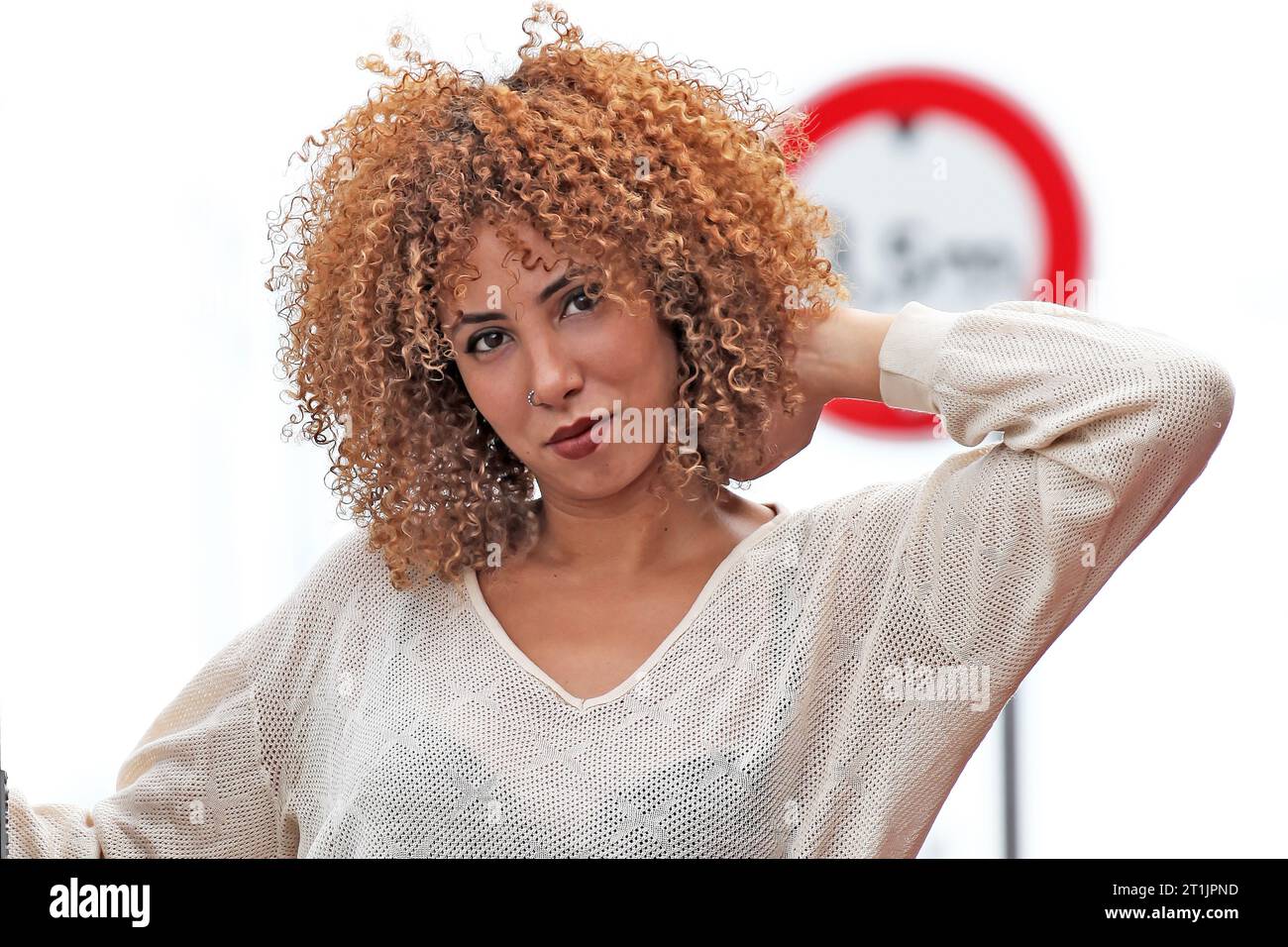 Outdoor portraits of a blond curly hair woman with a white sweater and red pants Stock Photo