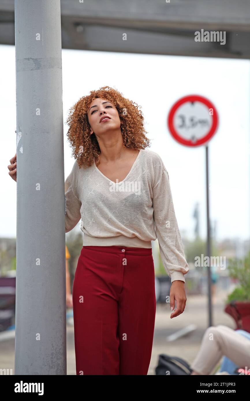 Outdoor portraits of a blond curly hair woman with a white sweater and red pants Stock Photo