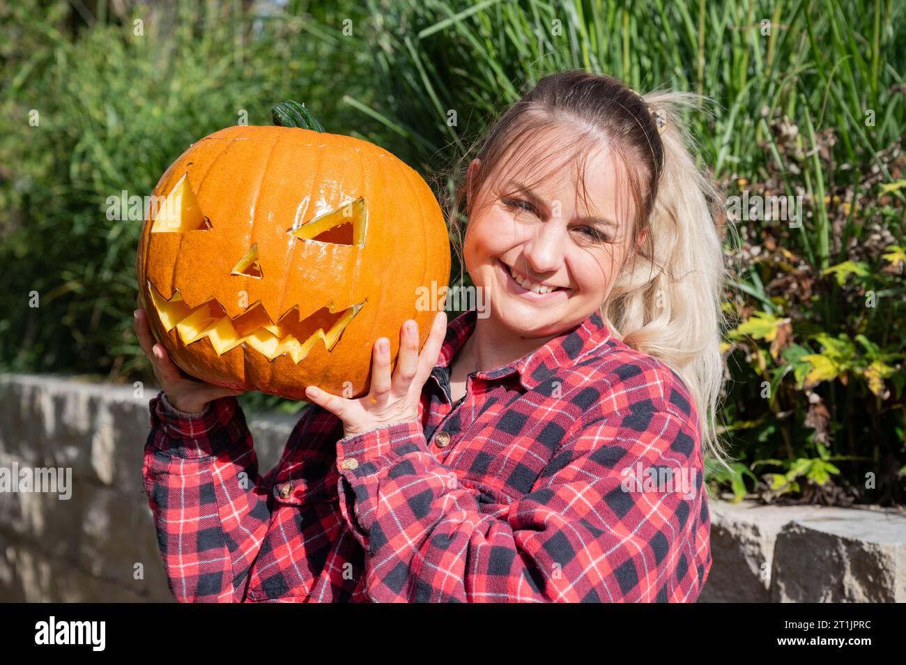Blonde woman in the garden presents a self-carved pumpkin with face as decoration for Halloween time Stock Photo