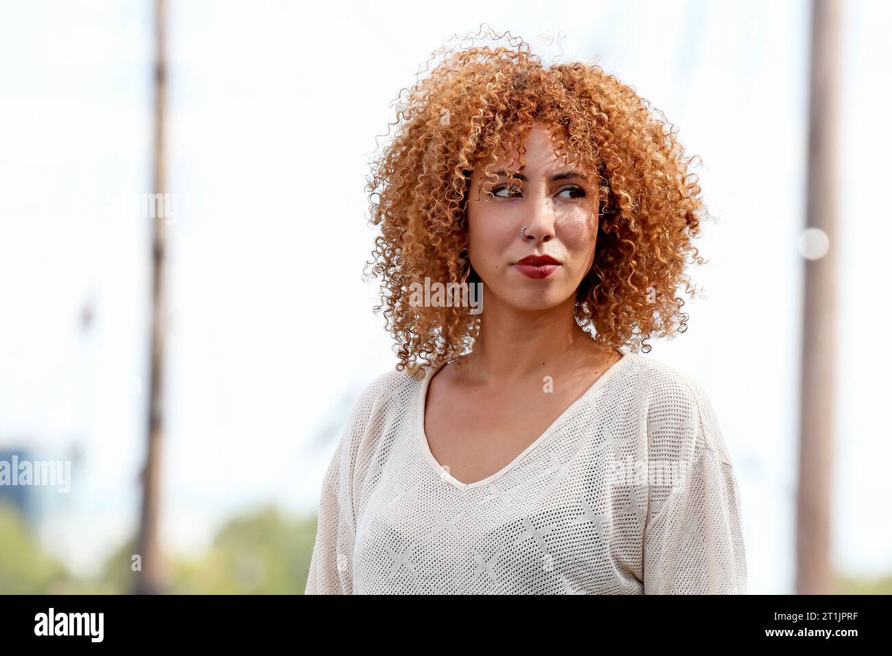 Outdoor portraits of a blond curly hair woman with a white sweater and red pants Stock Photo