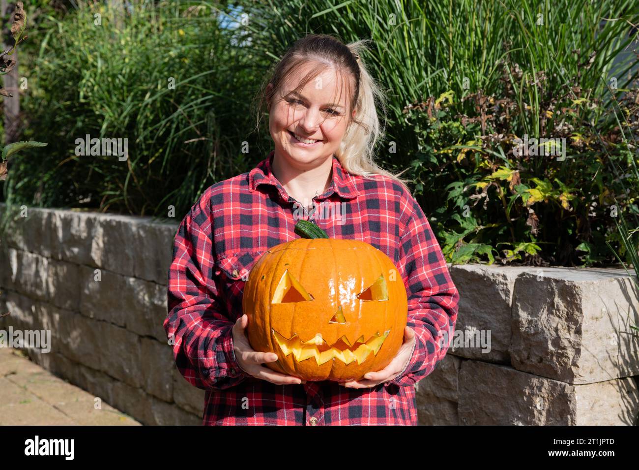 Blonde woman in the garden presents a self-carved pumpkin with face as decoration for Halloween time Stock Photo