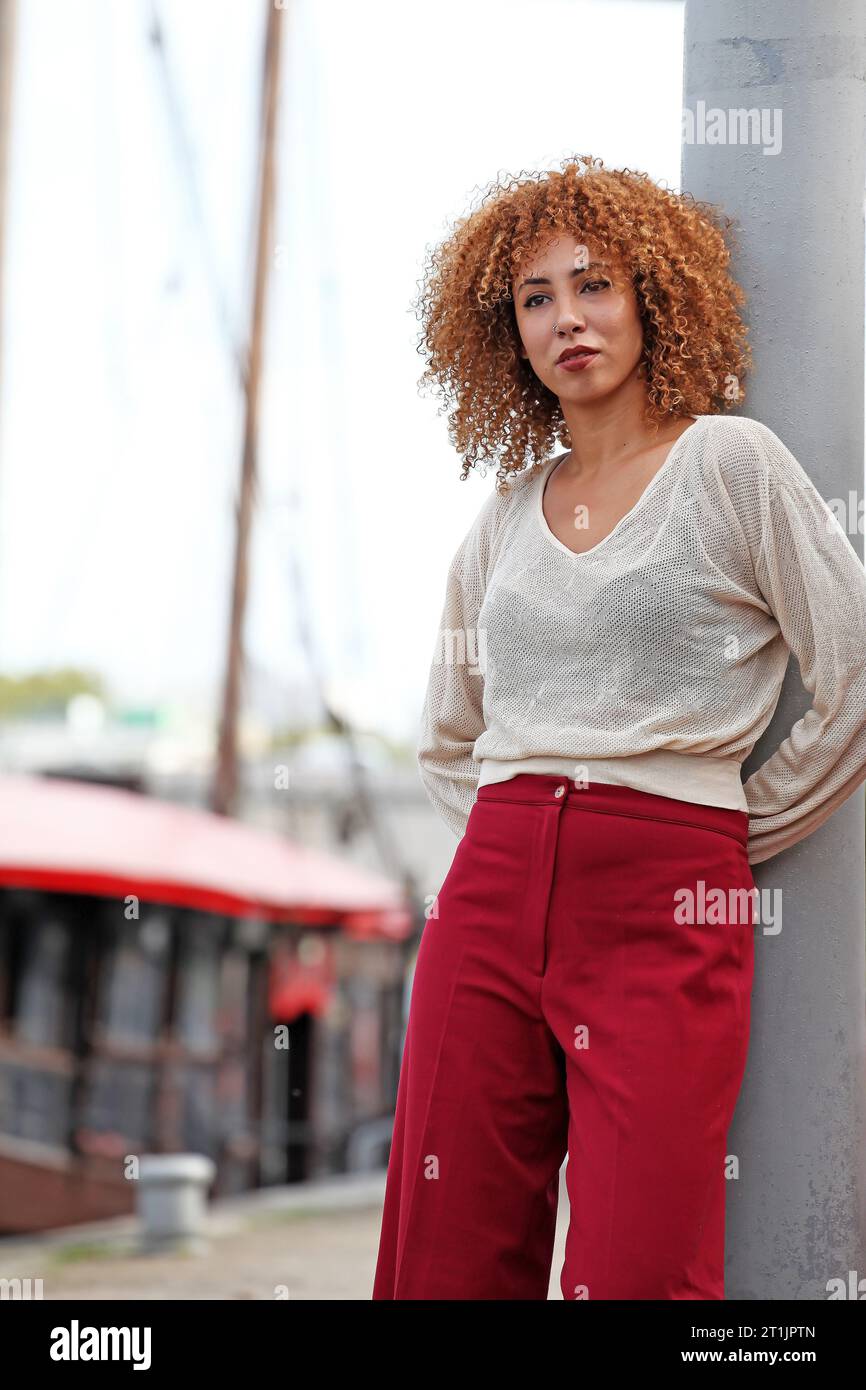 Outdoor portraits of a blond curly hair woman with a white sweater and red pants Stock Photo