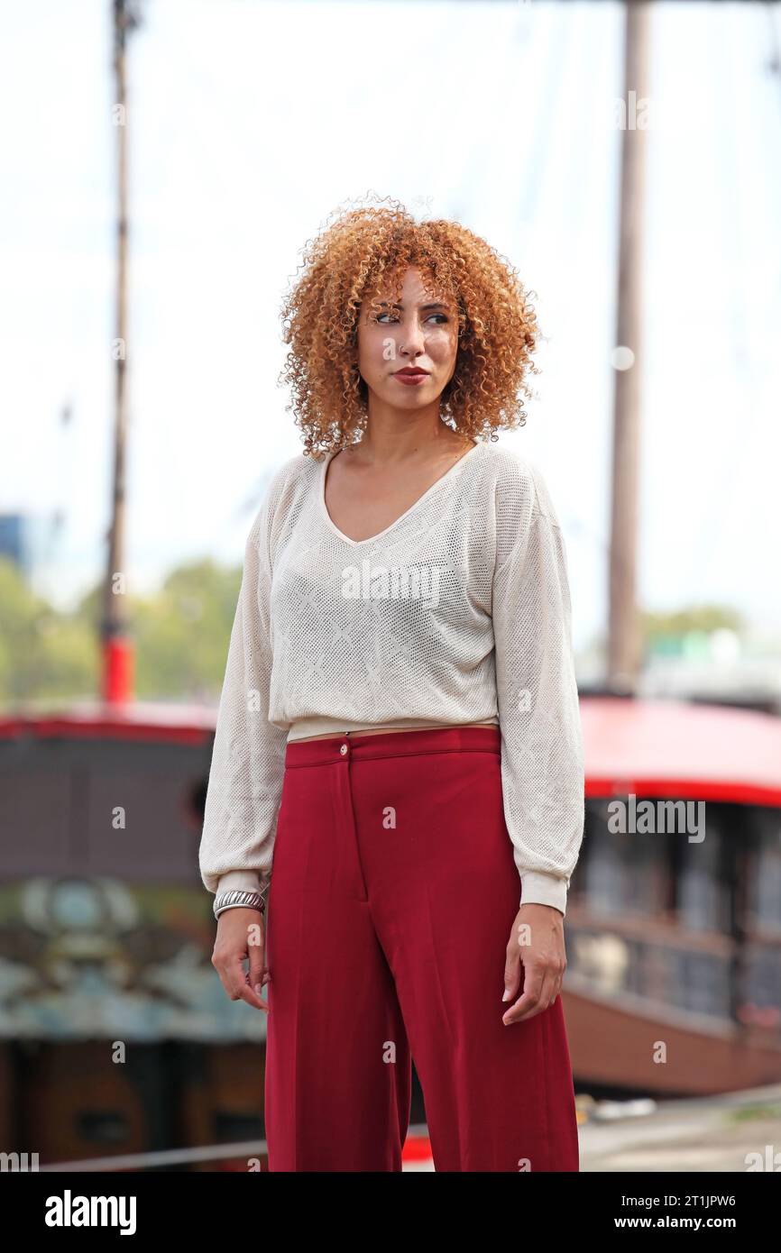 Outdoor portraits of a blond curly hair woman with a white sweater and red pants Stock Photo