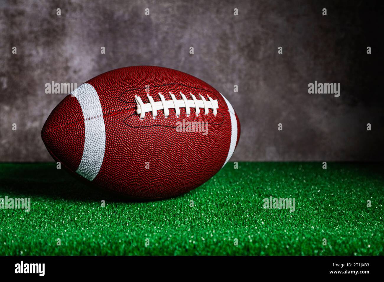 An american football ball over a ground with green grass in front of a concrete wall. Stock Photo