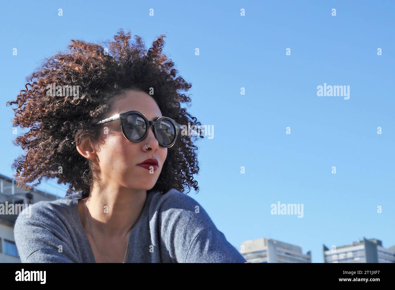 HEAD PORTRAIT OF A CURLY HAIR WOMAN WITH SUNGLASSES ON A HOT SUNNY DAY Stock Photo