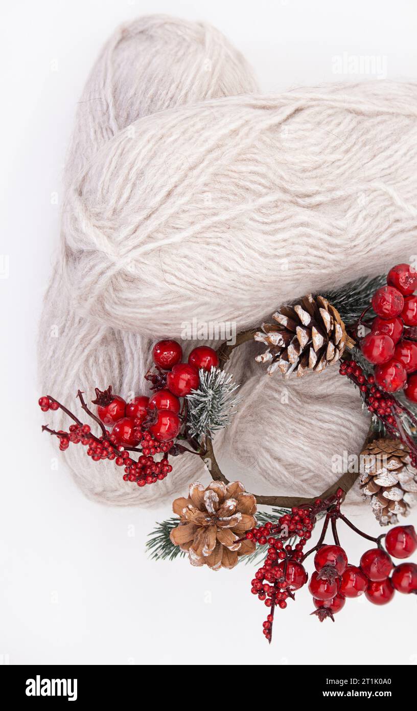 Gray woolen skeins or yarn of wool with branch of red berries and pine cones on white background. Handmade, knitting, hobby. Copy space Stock Photo